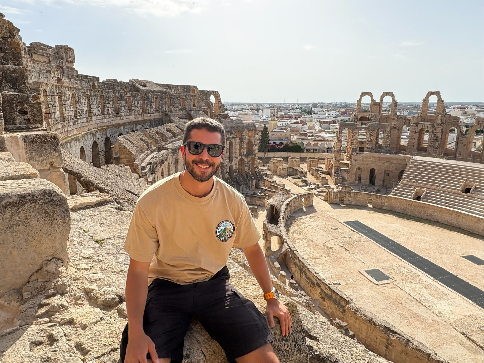 Tayssir sitting on the upper tiers of a Roman amphitheatre, the town visible beyond it.